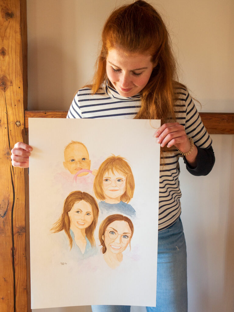 Malina Beye hält ein A2 Bild in den Händen. Darauf zu sehen sind 4 Porträts einer weiblichen Person. Sie wurden in Aquarellfarben gezeichnet